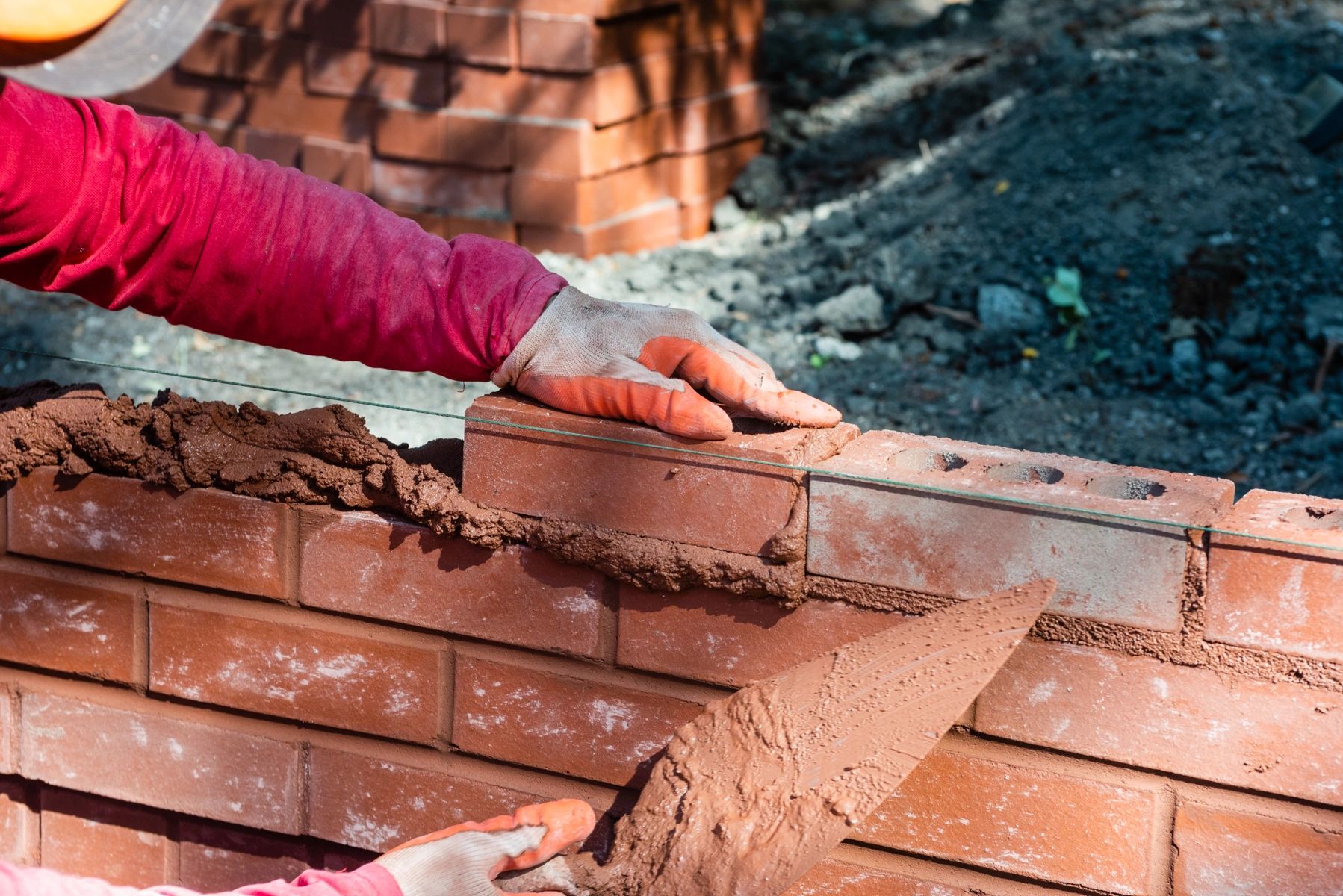 A mason setting a brick into fresh mortar along a guide line